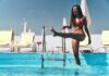 Enjoying summer day. Full length of playful young woman in red bikini splashing the water and smiling while standing in the swimming pool